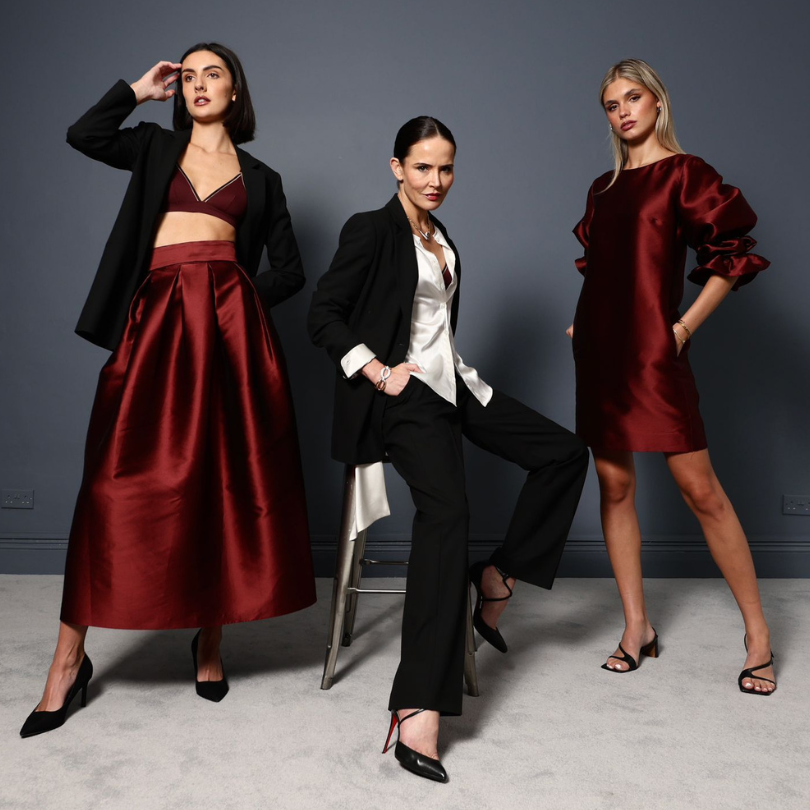 three women posed for the camera. Two are wearing oxblood - one in an A line skirt, the other in a short dress with puffball sleeves. Those are perfect Christmas outfits, while the lady in the centre (Sophie Anderton) wears elegant suiting.