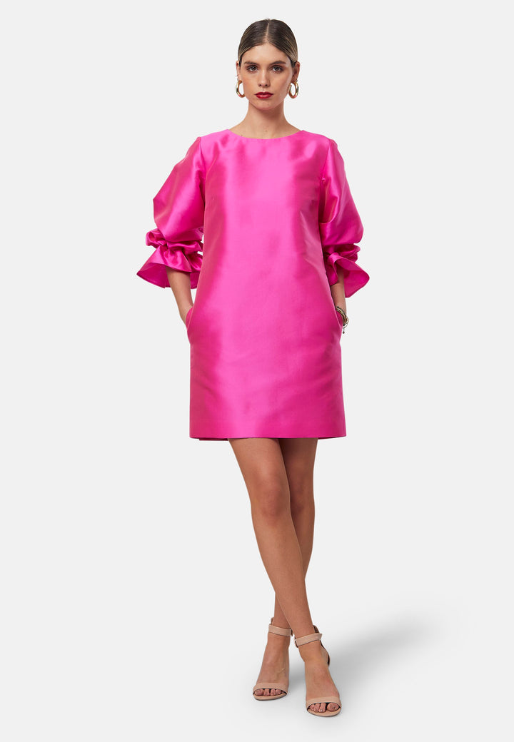 Step into the spotlight with Aurora, a chic short-shift dress in bold Fuchsia. This feminine piece features a statement double puff-ball sleeve, side seam pockets, and falls just above the knee. Crafted from a shimmering silk blend taffeta. Make a grand entrance with Aurora, perfect for a soiree or formal dressing.