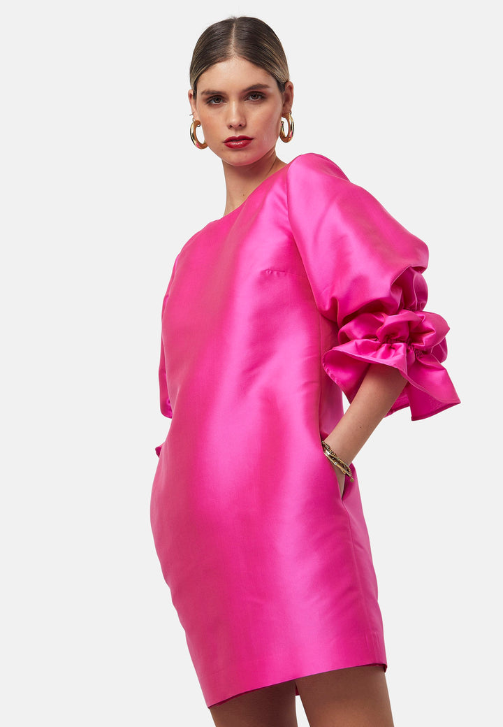 Step into the spotlight with Aurora, a chic short-shift dress in bold Fuchsia. This feminine piece features a statement double puff-ball sleeve, side seam pockets, and falls just above the knee. Crafted from a shimmering silk blend taffeta. Make a grand entrance with Aurora, perfect for a soiree or formal dressing.