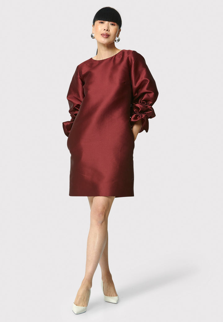 Step into the spotlight with Aurora, a chic short shift dress in a stunning mahogany red hue. This stylish piece features a statement puff-ball sleeve , side seam pockets, and falls above the knee. Crafted from a silk blend taffeta. Make a grand entrance with Aurora.