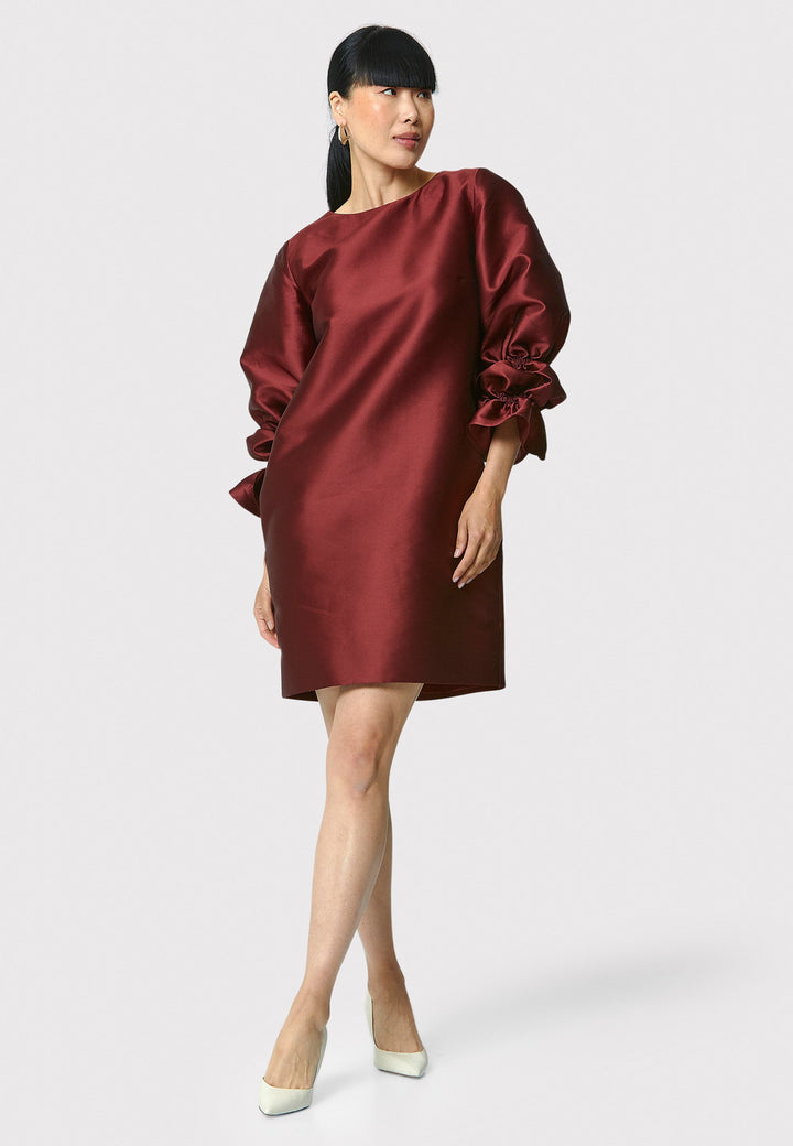 Step into the spotlight with Aurora, a chic short shift dress in a stunning mahogany red hue. This stylish piece features a statement puff-ball sleeve , side seam pockets, and falls above the knee. Crafted from a silk blend taffeta. Make a grand entrance with Aurora.