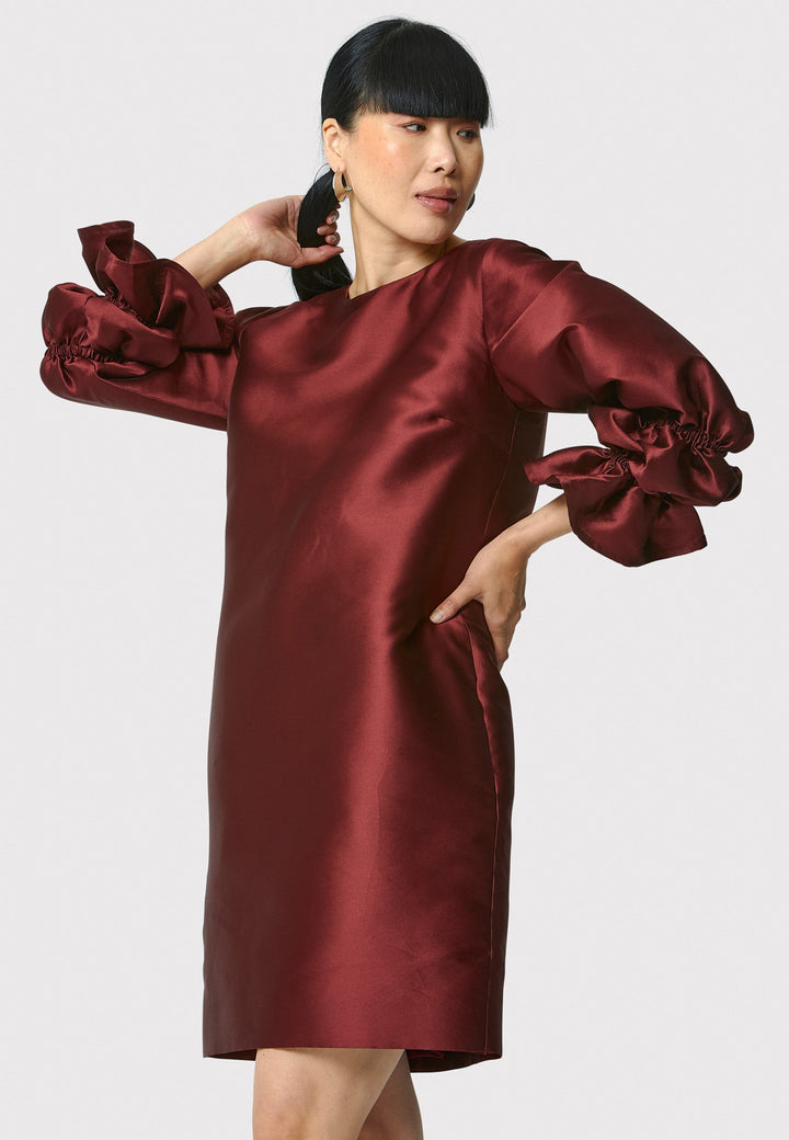 Step into the spotlight with Aurora, a chic short shift dress in a stunning mahogany red hue. This stylish piece features a statement puff-ball sleeve , side seam pockets, and falls above the knee. Crafted from a silk blend taffeta. Make a grand entrance with Aurora.