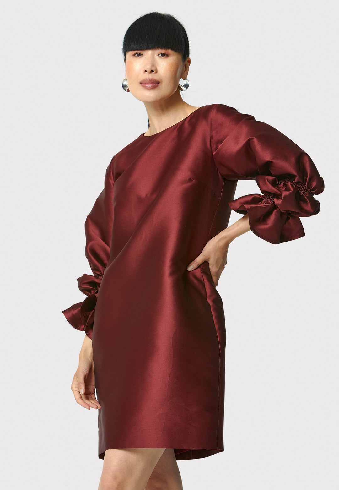 Step into the spotlight with Aurora, a chic short shift dress in a stunning mahogany red hue. This stylish piece features a statement puff-ball sleeve , side seam pockets, and falls above the knee. Crafted from a silk blend taffeta. Make a grand entrance with Aurora.