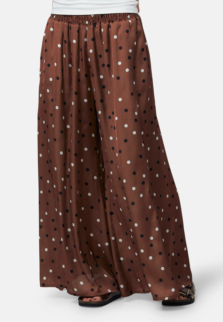 The Imogen wide-leg trousers in a brown base, black and white polkadot print. Prioritizing comfort with an elasticated gathered waistband. The pattern adds a touch of fun to this bestseller silhouette.