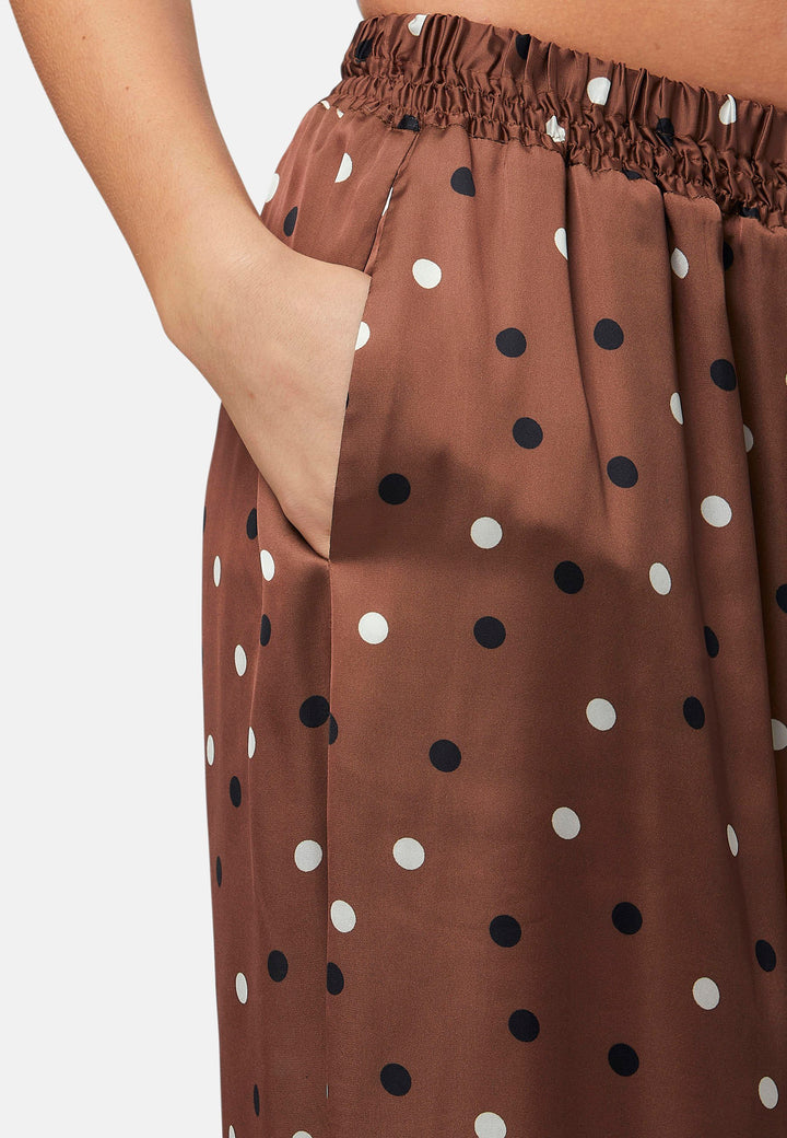 The Imogen wide-leg trousers in a brown base, black and white polkadot print. Prioritizing comfort with an elasticated gathered waistband. The pattern adds a touch of fun to this bestseller silhouette.