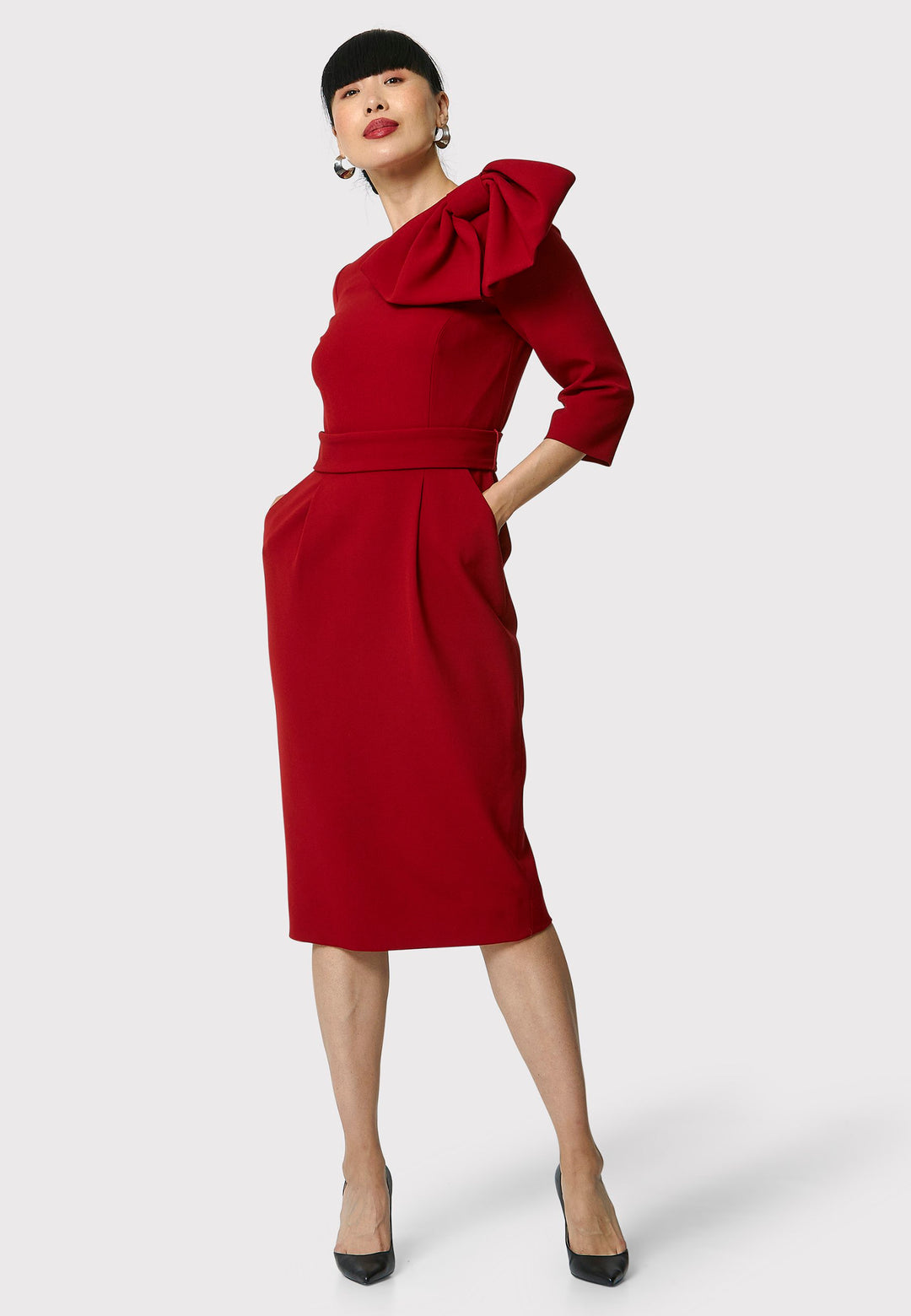 The Isadora Dress in garnet red, a body-skimming silhouette, featuring a slash neckline with a dramatic bow on the shoulder. The dress falls to the mid-calf and back vent ensure ease of movement. Crafted from a fabric blend with a hint of stretch, it offers a comfortable and flattering fit. Ideal for evening cocktails, a night at the theatre, or a stylish winter wedding.