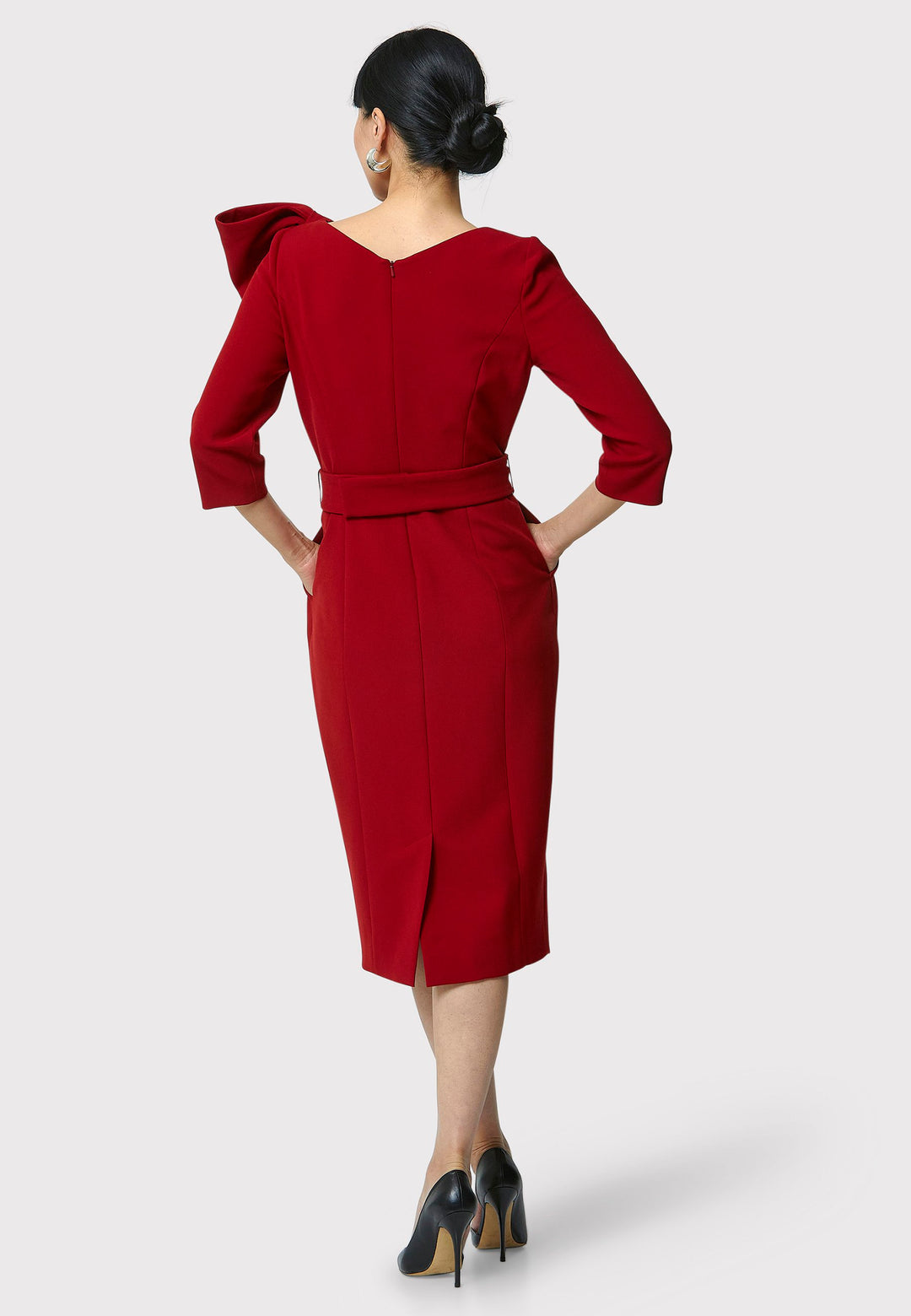 The Isadora Dress in garnet red, a body-skimming silhouette, featuring a slash neckline with a dramatic bow on the shoulder. The dress falls to the mid-calf and back vent ensure ease of movement. Crafted from a fabric blend with a hint of stretch, it offers a comfortable and flattering fit. Ideal for evening cocktails, a night at the theatre, or a stylish winter wedding.