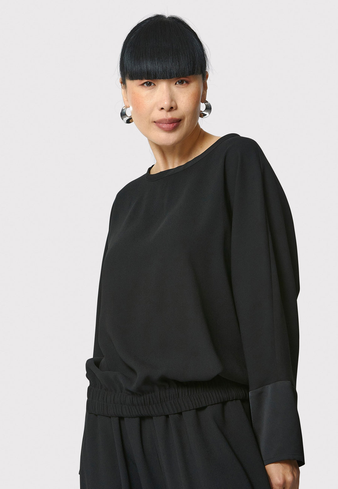 Lal, black top in fluid satin back crepe. A relaxed fit, elastic waistband, Dropped Shoulder sleeves, and satin cuffs. Wear with the coordinating Deliliah or Imogen Pant.