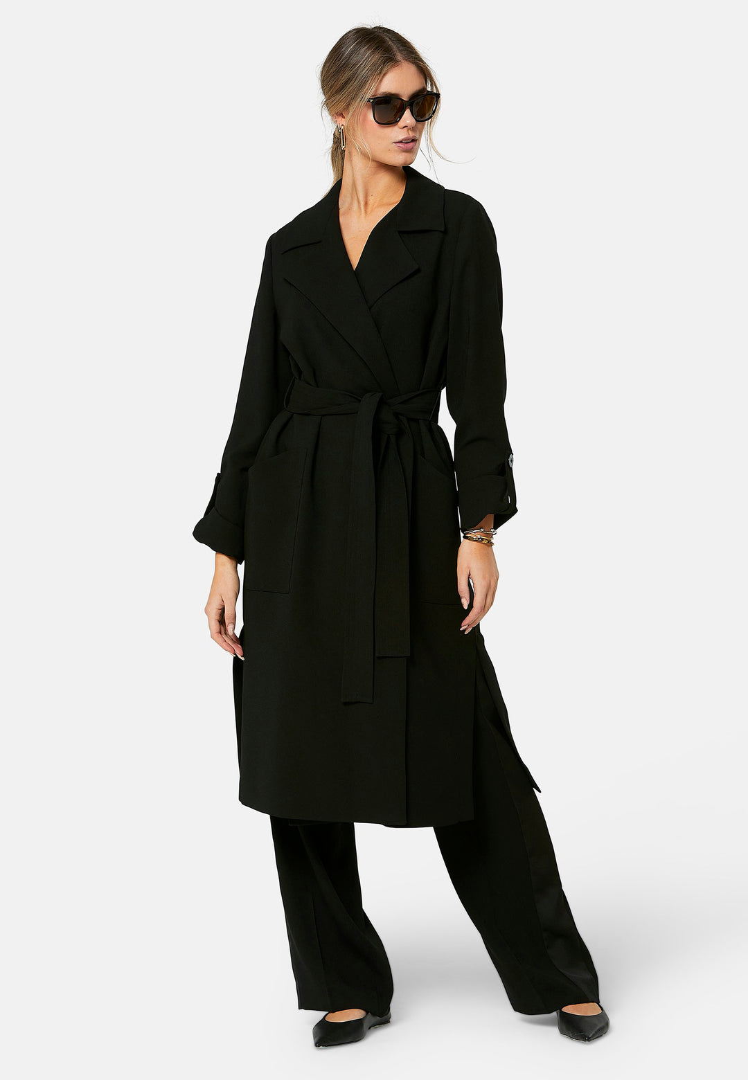 Lydiah, black trench coat in a fluid satin back crepe. This coat features a relaxed, flowing silhouette, a self-tie belt, and front pockets. The design includes buttoned cuffs and a wide lapel. Pair with coordinating trouser for a chic monochromatic look.