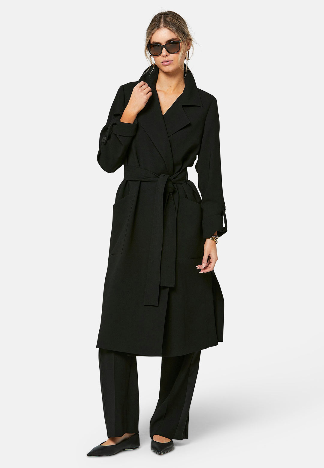 Lydiah, black trench coat in a fluid satin back crepe. This coat features a relaxed, flowing silhouette, a self-tie belt, and front pockets. The design includes buttoned cuffs and a wide lapel. Pair with coordinating trouser for a chic monochromatic look.