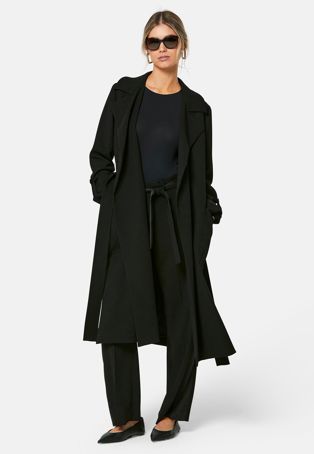 Lydiah, black trench coat in a fluid satin back crepe. This coat features a relaxed, flowing silhouette, a self-tie belt, and front pockets. The design includes buttoned cuffs and a wide lapel. Pair with coordinating trouser for a chic monochromatic look.