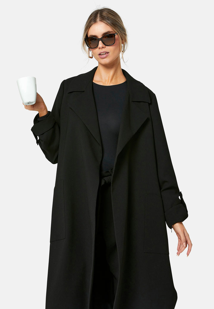 Lydiah, black trench coat in a fluid satin back crepe. This coat features a relaxed, flowing silhouette, a self-tie belt, and front pockets. The design includes buttoned cuffs and a wide lapel. Pair with coordinating trouser for a chic monochromatic look.