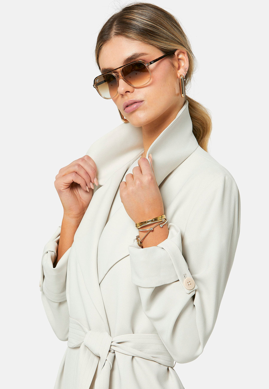 Lydiah, stone trench coat in a fluid satin back crepe. This coat features a relaxed, flowing silhouette, a self-tie belt, and front pockets. The design includes buttoned cuffs and a wide lapel. Pair with coordinating trouser for a chic monochromatic look.