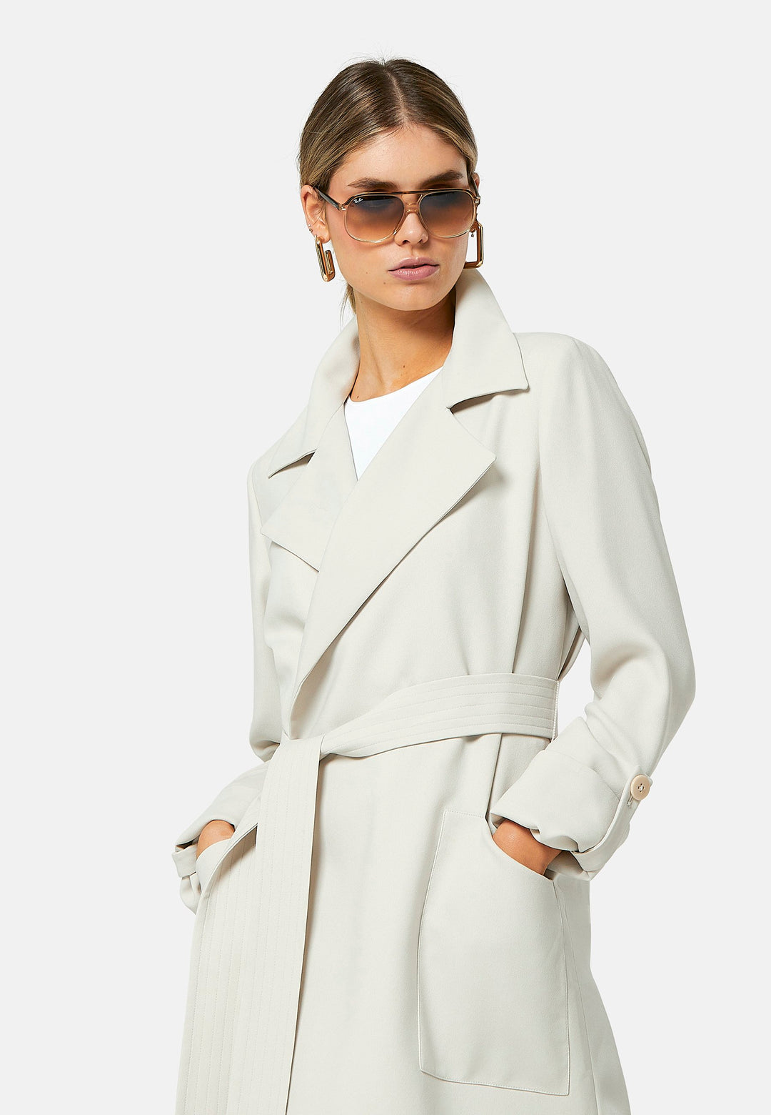 Lydiah, stone trench coat in a fluid satin back crepe. This coat features a relaxed, flowing silhouette, a self-tie belt, and front pockets. The design includes buttoned cuffs and a wide lapel. Pair with coordinating trouser for a chic monochromatic look.