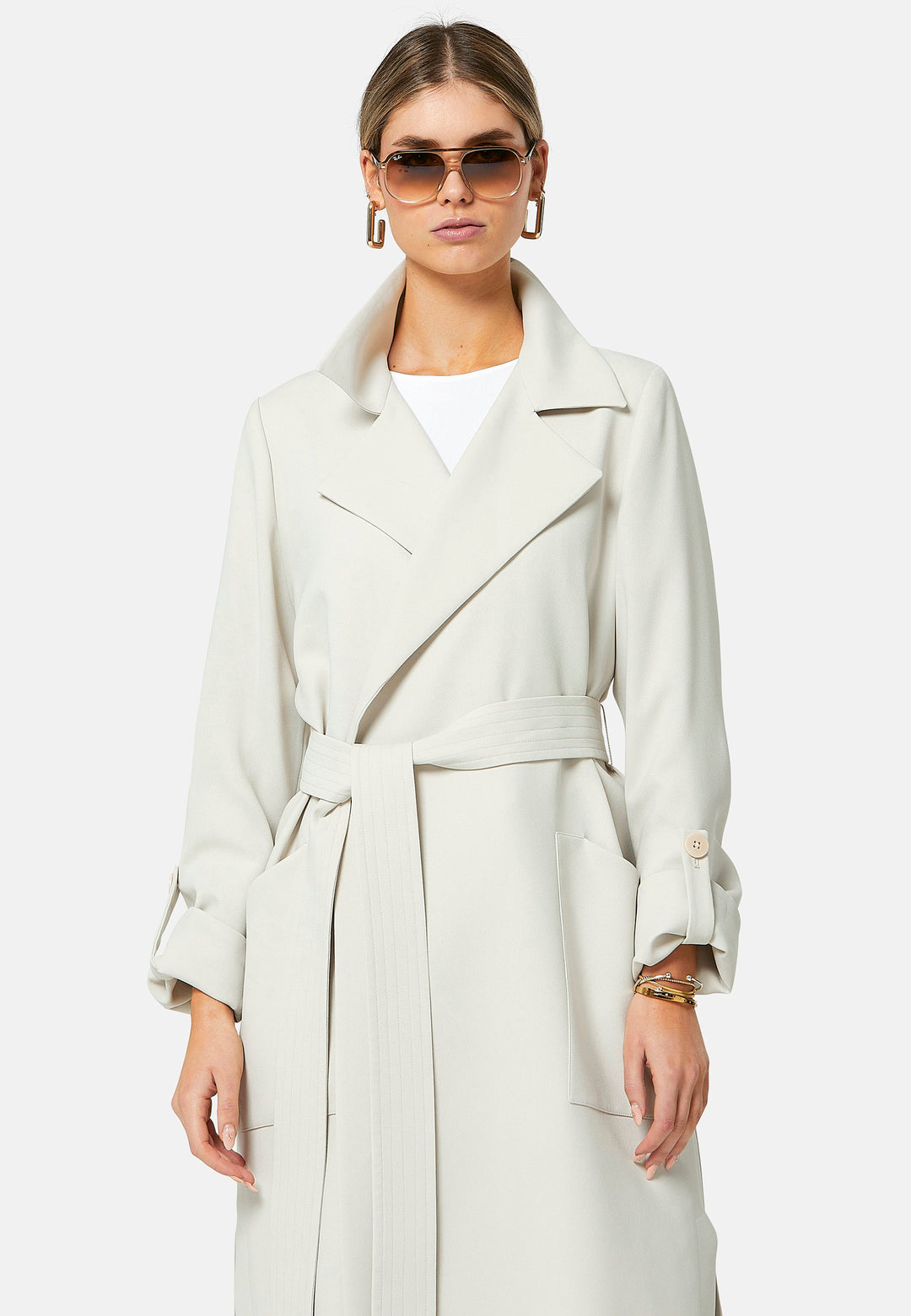 Lydiah, stone trench coat in a fluid satin back crepe. This coat features a relaxed, flowing silhouette, a self-tie belt, and front pockets. The design includes buttoned cuffs and a wide lapel. Pair with coordinating trouser for a chic monochromatic look.