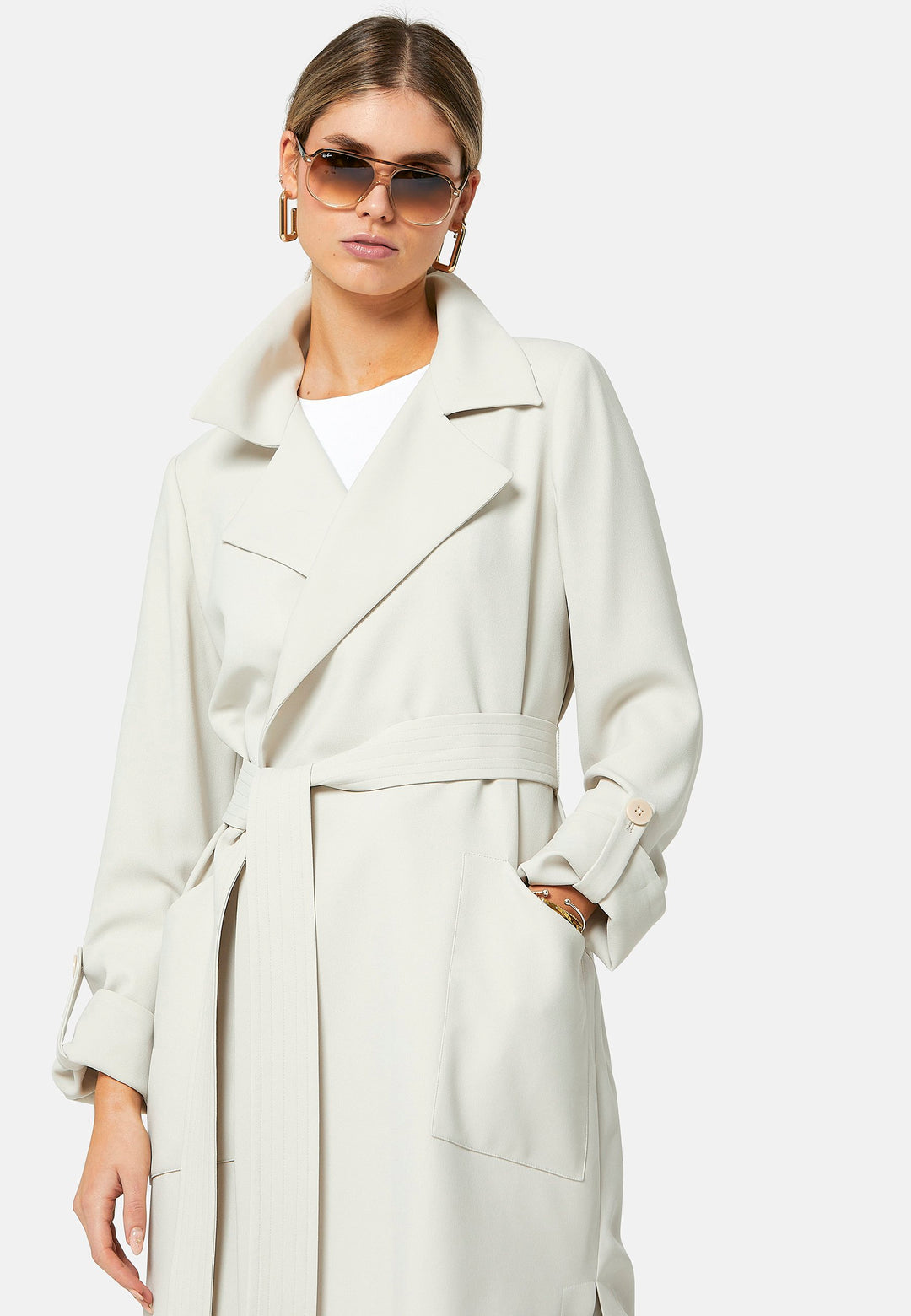 Lydiah, stone trench coat in a fluid satin back crepe. This coat features a relaxed, flowing silhouette, a self-tie belt, and front pockets. The design includes buttoned cuffs and a wide lapel. Pair with coordinating trouser for a chic monochromatic look.