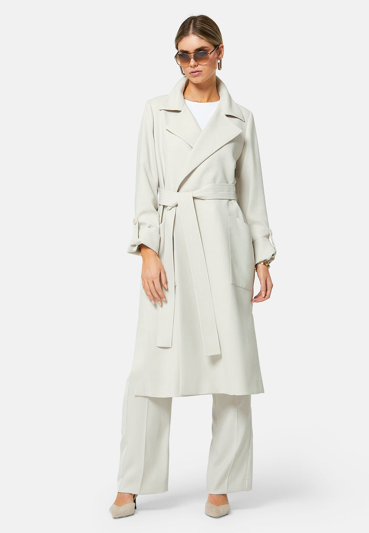 Lydiah, stone trench coat in a fluid satin back crepe. This coat features a relaxed, flowing silhouette, a self-tie belt, and front pockets. The design includes buttoned cuffs and a wide lapel. Pair with coordinating trouser for a chic monochromatic look.