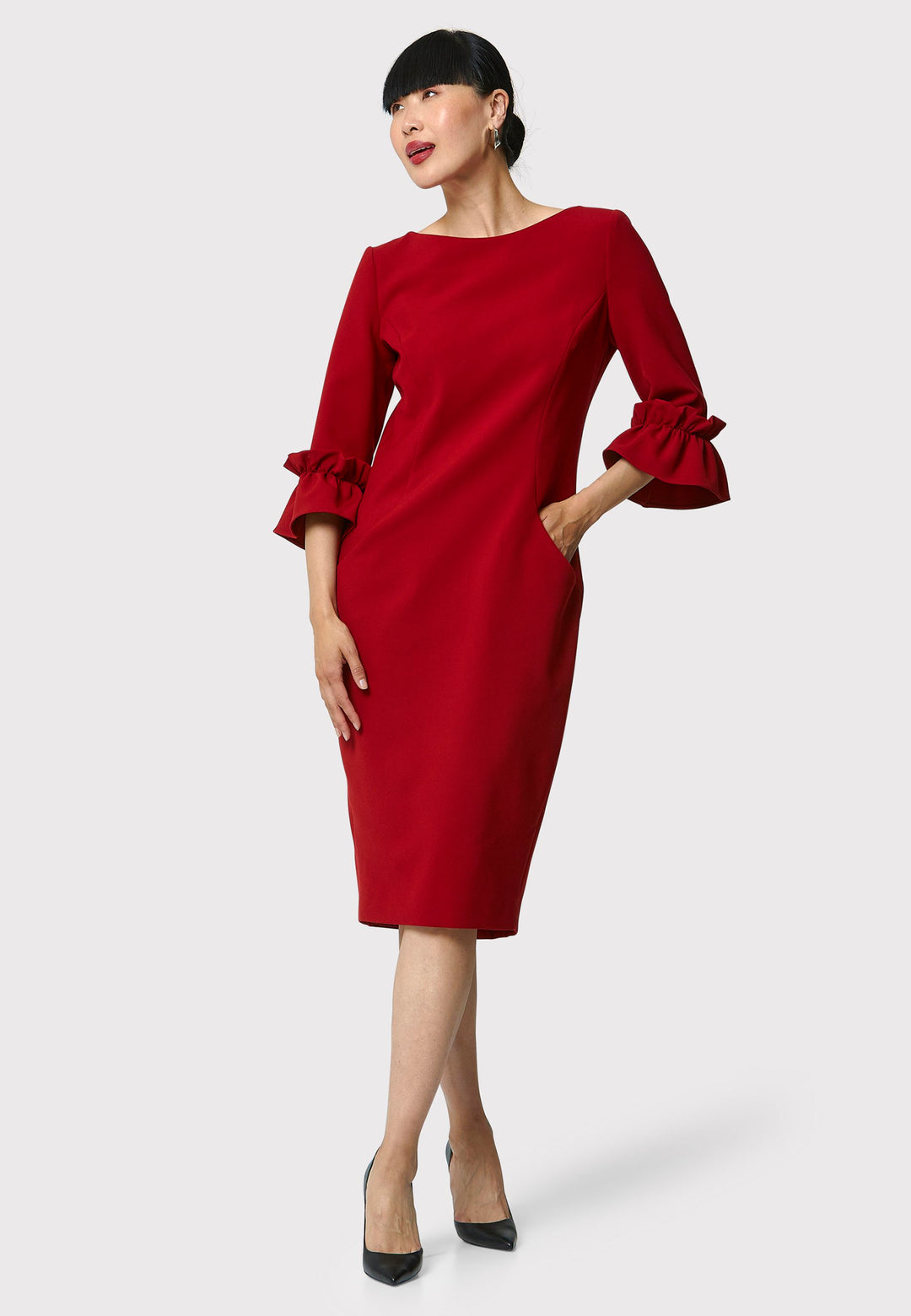 The Maisie Garnet Red Dress, impeccably tailored from signature tricotine fabric with a hint of stretch. This body-skimming silhouette features a round neck and bracelet-length sleeves complemented by exaggerated frill cuffs, ideal for evening cocktails, a night at the theatre, or a stylish winter wedding.