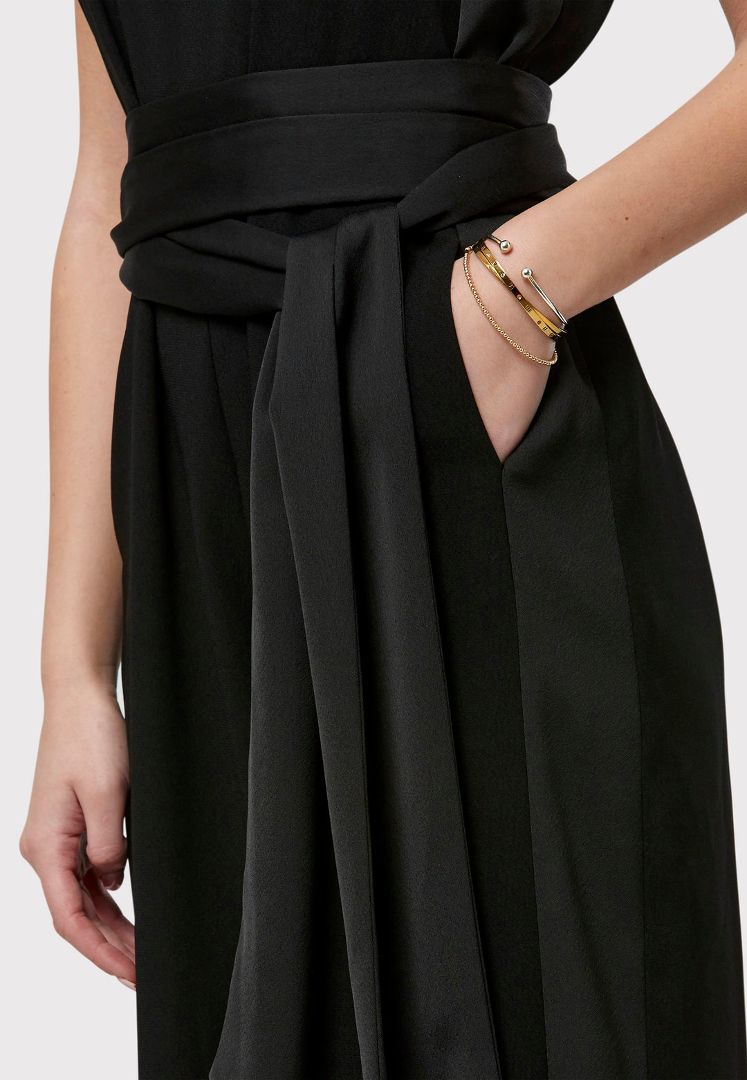 Marie-Claire, a sleeveless black jumpsuit in fluid satin back crepe. Featuring a wide-leg silhouette and satin stripes on the side seams. It comes with a detachable self-fabric belt that can be used to cinch the waist or worn around the neck. Includes practical side pockets for added convenience. Perfect for relaxed yet sophisticated evening dressing.