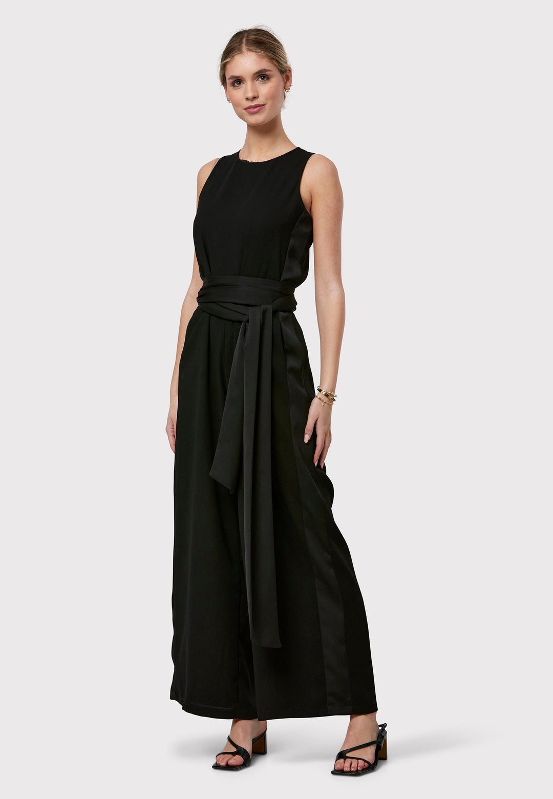 Marie-Claire, a sleeveless black jumpsuit in fluid satin back crepe. Featuring a wide-leg silhouette and satin stripes on the side seams. It comes with a detachable self-fabric belt that can be used to cinch the waist or worn around the neck. Includes practical side pockets for added convenience. Perfect for relaxed yet sophisticated evening dressing.