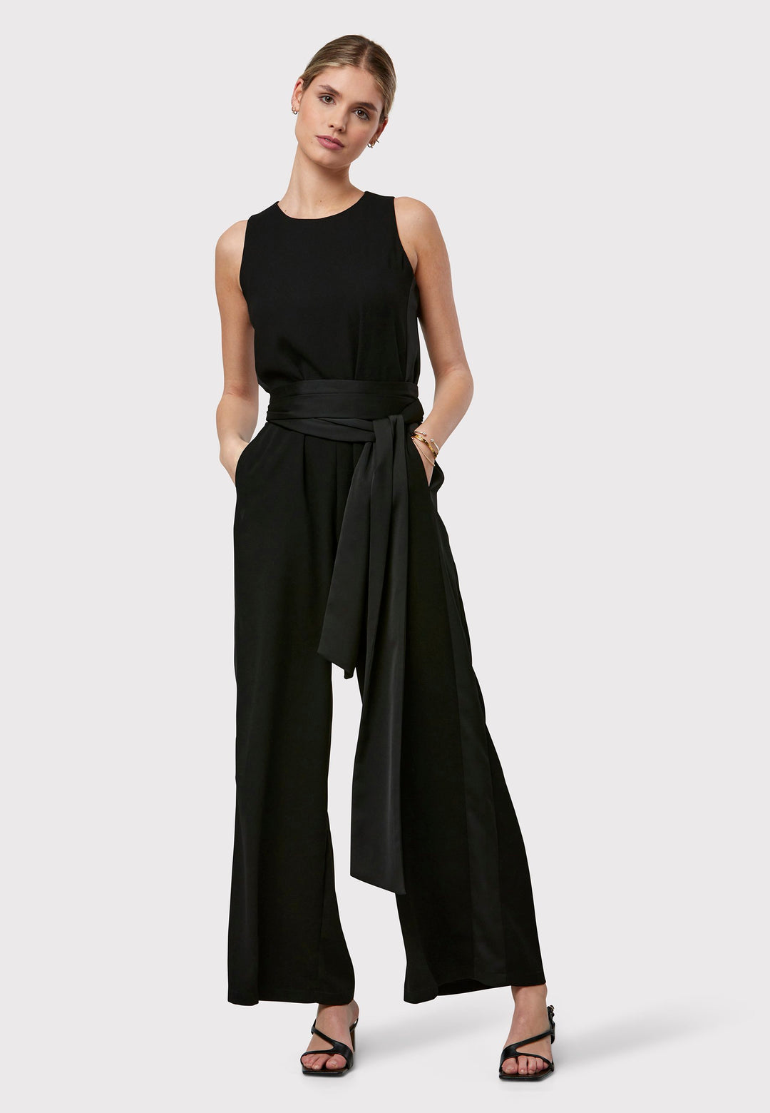 Marie-Claire, a sleeveless black jumpsuit in fluid satin back crepe. Featuring a wide-leg silhouette and satin stripes on the side seams. It comes with a detachable self-fabric belt that can be used to cinch the waist or worn around the neck. Includes practical side pockets for added convenience. Perfect for relaxed yet sophisticated evening dressing.