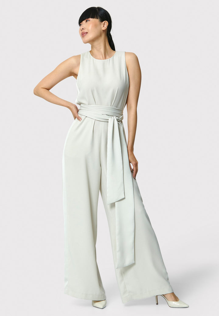 Marie-Claire, a sleeveless stone jumpsuit in fluid satin back crepe. Featuring a wide-leg silhouette and satin stripes on the side seams. It comes with a detachable self-fabric belt that can be used to cinch the waist or worn around the neck. Includes practical side pockets for added convenience. Perfect for relaxed yet sophisticated evening dressing.