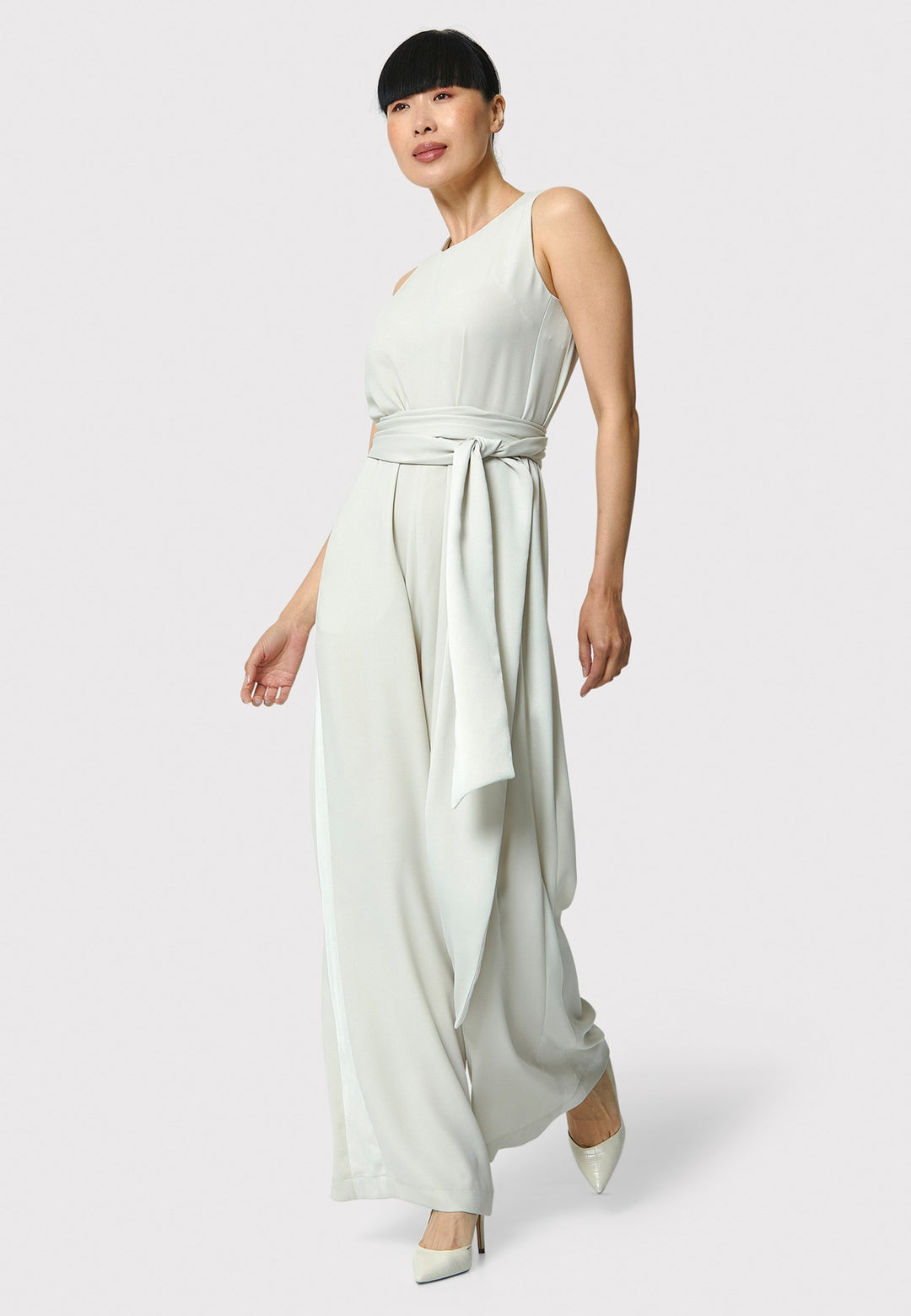 Marie-Claire, a sleeveless stone jumpsuit in fluid satin back crepe. Featuring a wide-leg silhouette and satin stripes on the side seams. It comes with a detachable self-fabric belt that can be used to cinch the waist or worn around the neck. Includes practical side pockets for added convenience. Perfect for relaxed yet sophisticated evening dressing.