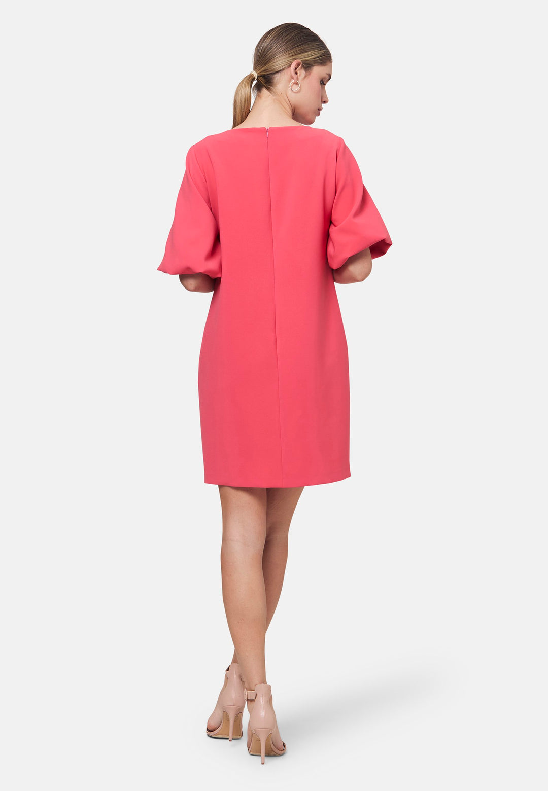 Mia, a chic short-shift dress in a fun watermelon pink hue. This feminine piece features a timeless silhouette with voluminous three-quarter puff sleeves and a round neckline. Its clean lines and relaxed fit make it ideal for both daytime outings and evening occasions.