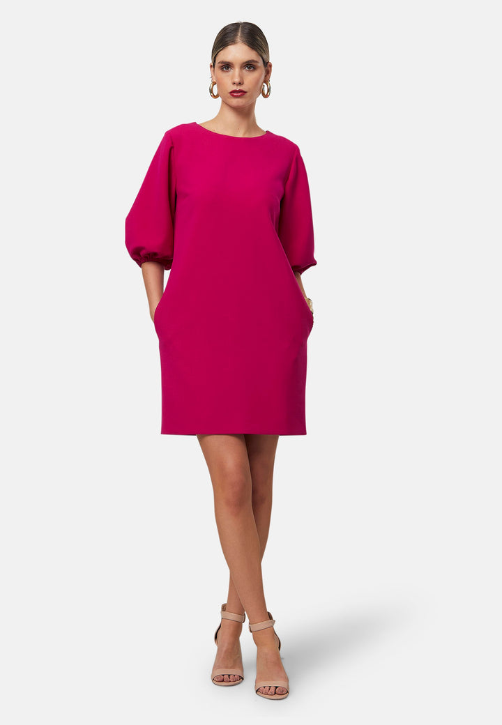 Mila, a chic short-shift dress in bold Fuchsia. This feminine piece features a timeless silhouette with voluminous three-quarter puff sleeves and a round neckline.