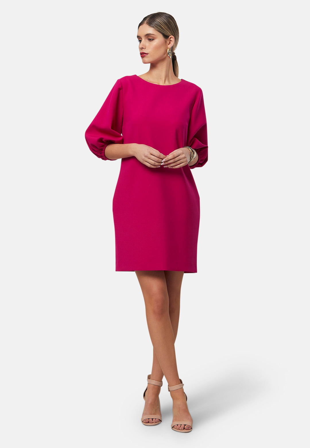 Mila, a chic short-shift dress in bold Fuchsia. This feminine piece features a timeless silhouette with voluminous three-quarter puff sleeves and a round neckline.