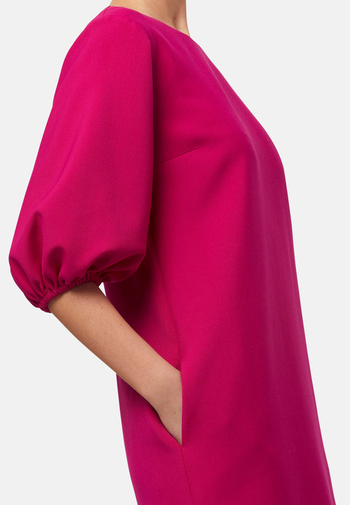 Mila, a chic short-shift dress in bold Fuchsia. This feminine piece features a timeless silhouette with voluminous three-quarter puff sleeves and a round neckline.