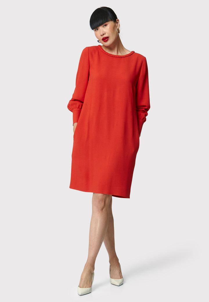 The Rachel Shift Dress is crafted in a vibrant burnt orange acetate and viscose blend crepe. This modern shift dress features a round neckline trimmed with an elegant plait trim. The relaxed-fit sleeves gather softly into buttoned cuffs, adding a refined touch. With convenient side pockets and a knee-length skirt, this dress is both stylish and practical. Perfect for work, wine or dining.