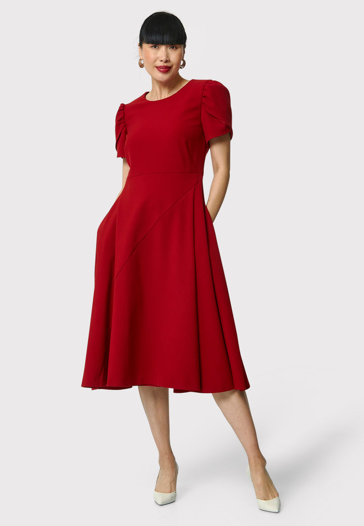 The Vera Garnet Red Dress is perfect for special occasions. It features a flattering fit-and-flare silhouette, a round neckline, and short puffed sleeves. The mid-calf length skirt flares out gracefully, adding elegance to the dress. Crafted from a comfortable fabric blend, it ensures ease of movement and a polished look.