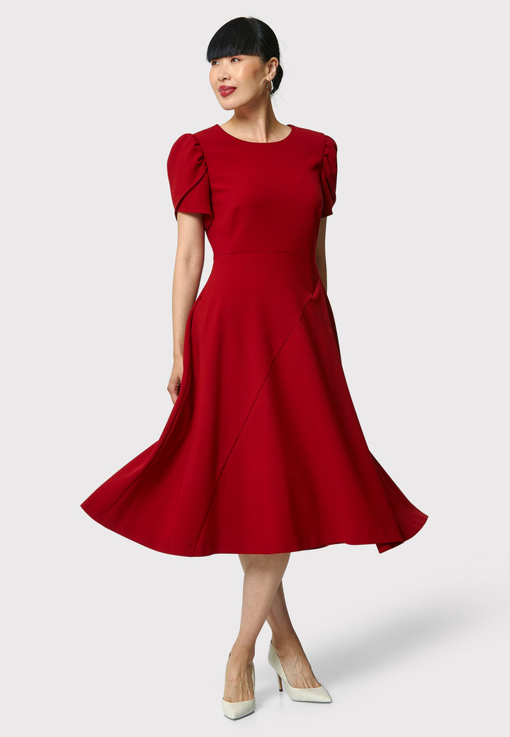 The Vera Garnet Red Dress is perfect for special occasions. It features a flattering fit-and-flare silhouette, a round neckline, and short puffed sleeves. The mid-calf length skirt flares out gracefully, adding elegance to the dress. Crafted from a comfortable fabric blend, it ensures ease of movement and a polished look.